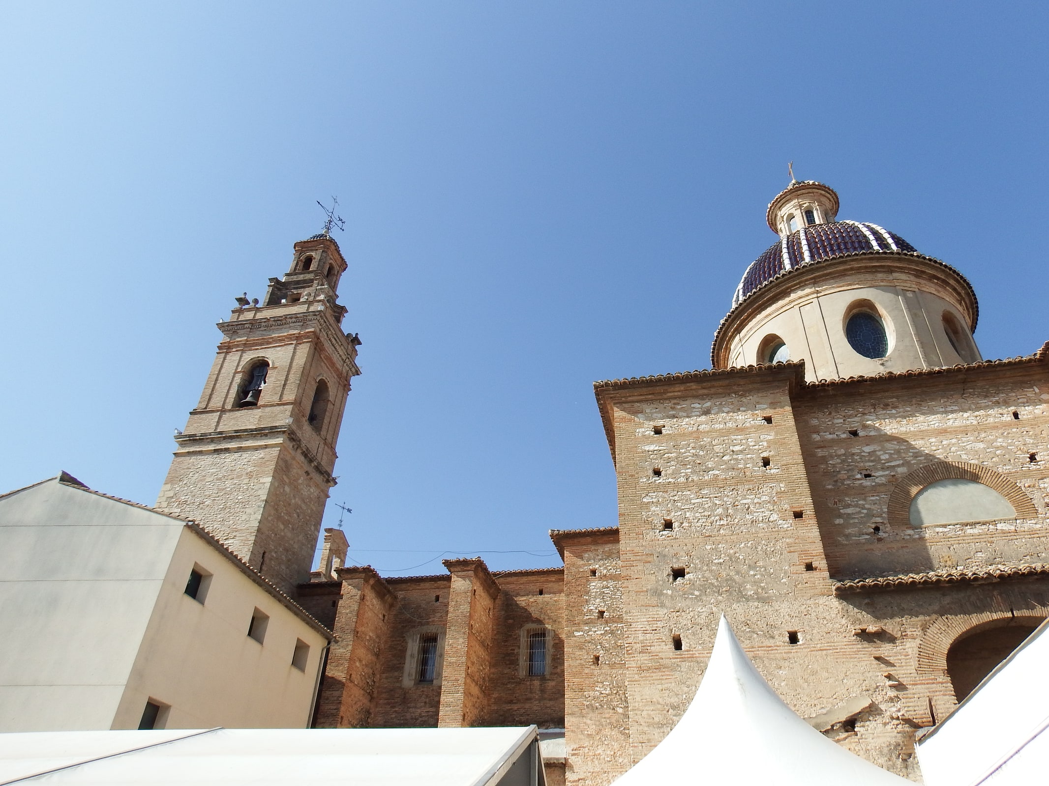 Bell tower, tiled dome, and brick-and-stone exterior of the Church of Our Lady of the Angels in Silla, Spain, beneath a clear blue sky.