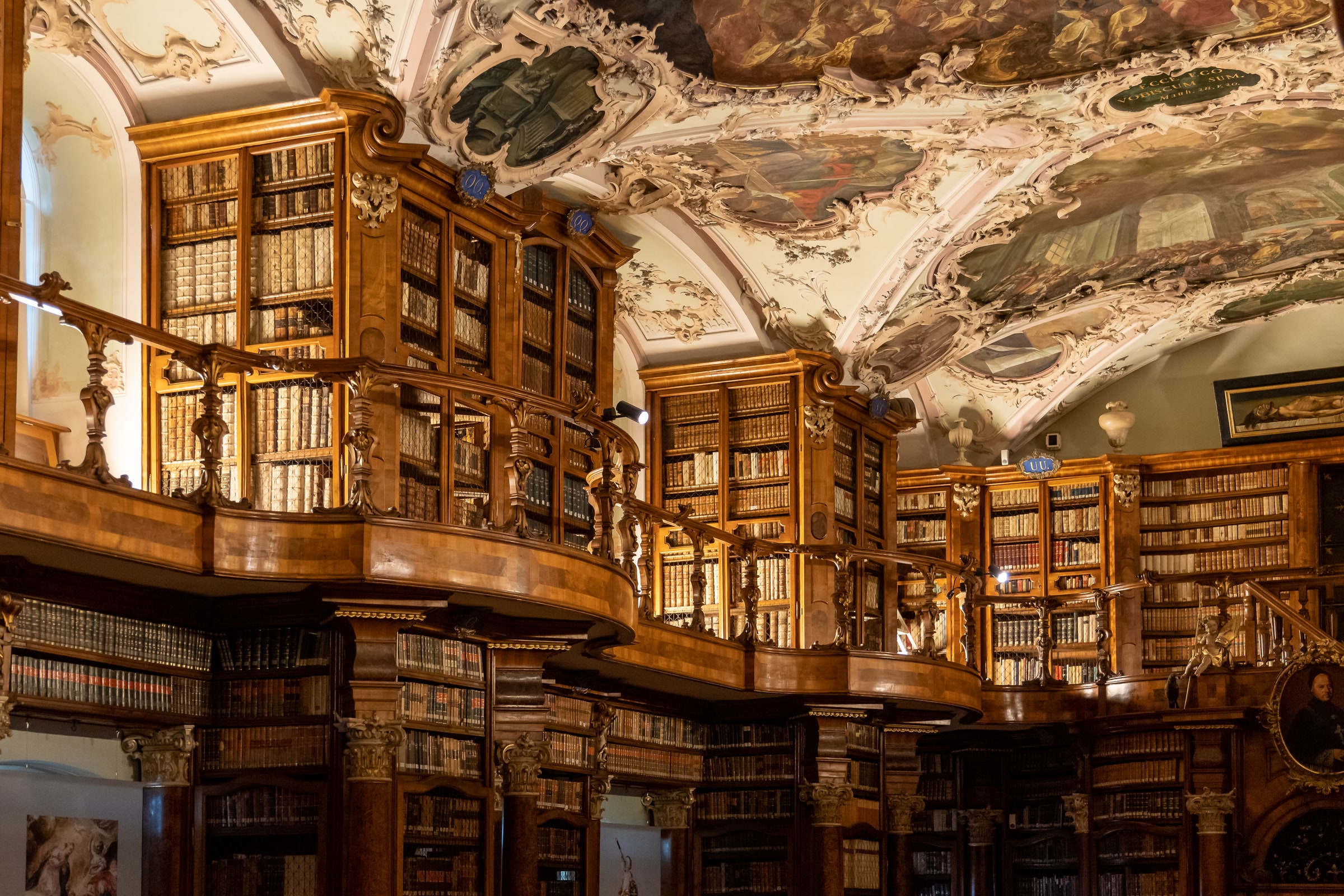 The curved wooden galleries, frescoed ceiling, and manuscript shelves of the Rococo Abbey Library hall in St. Gallen, Switzerland.